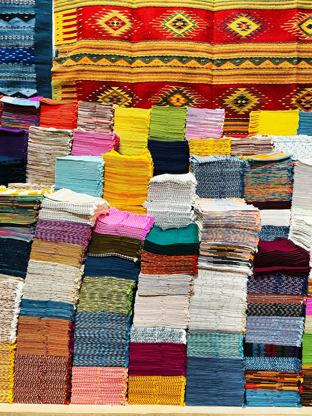 Stacks of colorful, patterned, handwoven textiles and rugs.